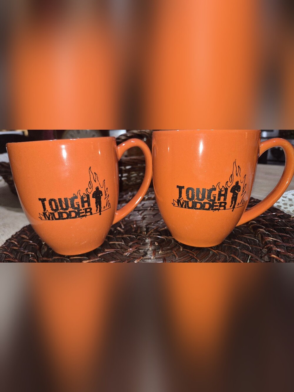 2 bright orange ceramic coffee mugs featuring the black "Tough Mudder" Logo